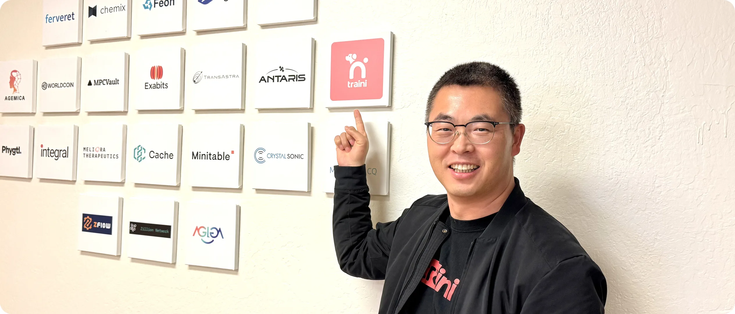 A Traini team member pointing at the Traini logo on a wall of startup logos